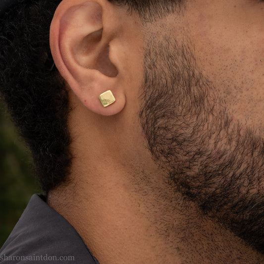 Solid 18k gold stud earrings 7mm square. Hammered with matte brushed finish, solid 18k gold posts and locking backs. Handcrafted in the USA by Sharon Saint Don. Worn by a man with dark skin, black hair and beard.