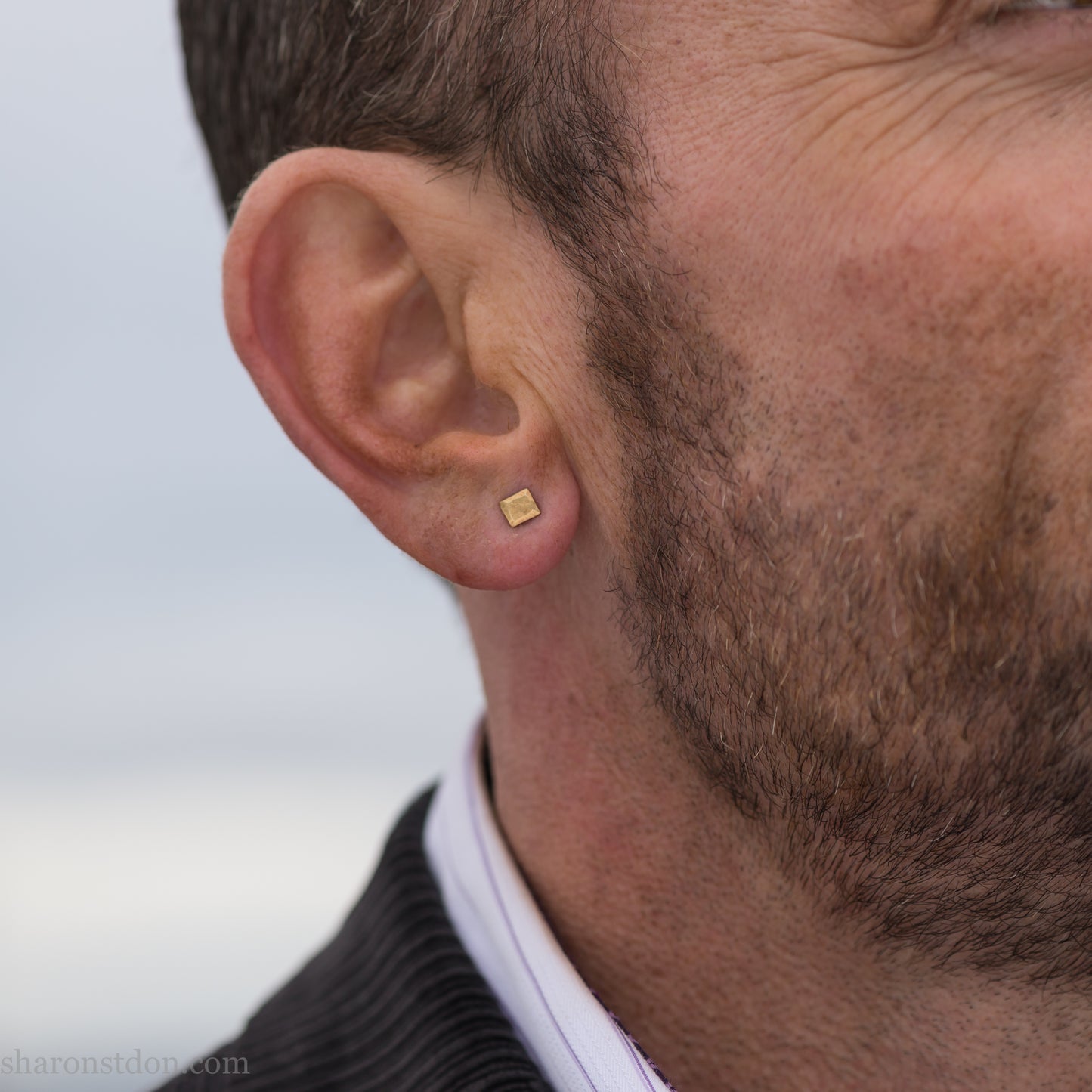 Handmade 22k gold and oxidized sterling silver stud earrings. 7mm square with hammered, matte texture finish. Handmade by Sharon Saint Don in USA. pictured on a man with brown hair, brown beard and fair skin.