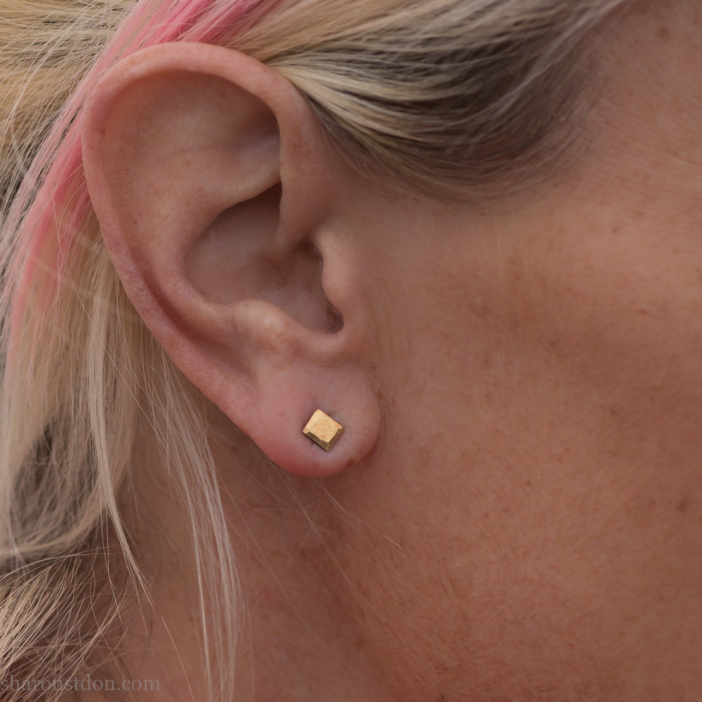 Handmade 22k gold and oxidized sterling silver stud earrings. 7mm square with hammered, matte texture finish. Handmade by Sharon Saint Don in USA. Pictured on a woman with blonde hair and fair skin.