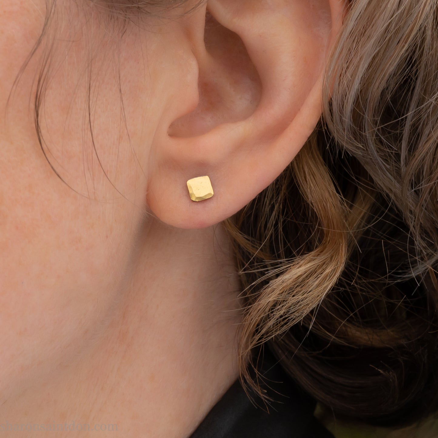 Handmade 22k gold and oxidized sterling silver stud earrings. 7mm square with hammered, matte texture finish. Handmade by Sharon Saint Don in USA. pictured on a person with light brown wavy hair, and fair skin.