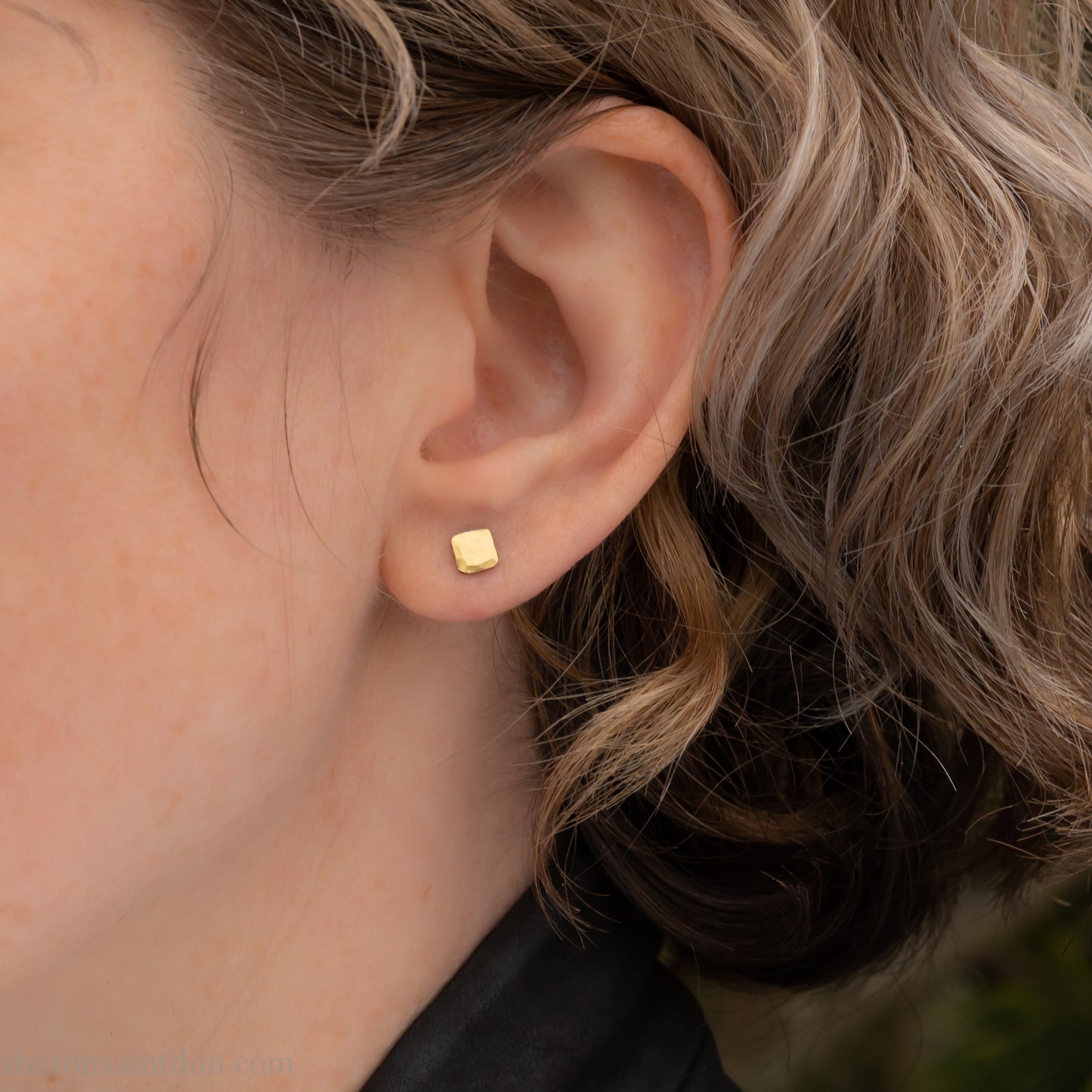 Handmade 22k gold and oxidized sterling silver stud earrings. 7mm square with hammered, matte texture finish. Handmade by Sharon Saint Don in USA. pictured on a person with light brown wavy hair, and fair skin.