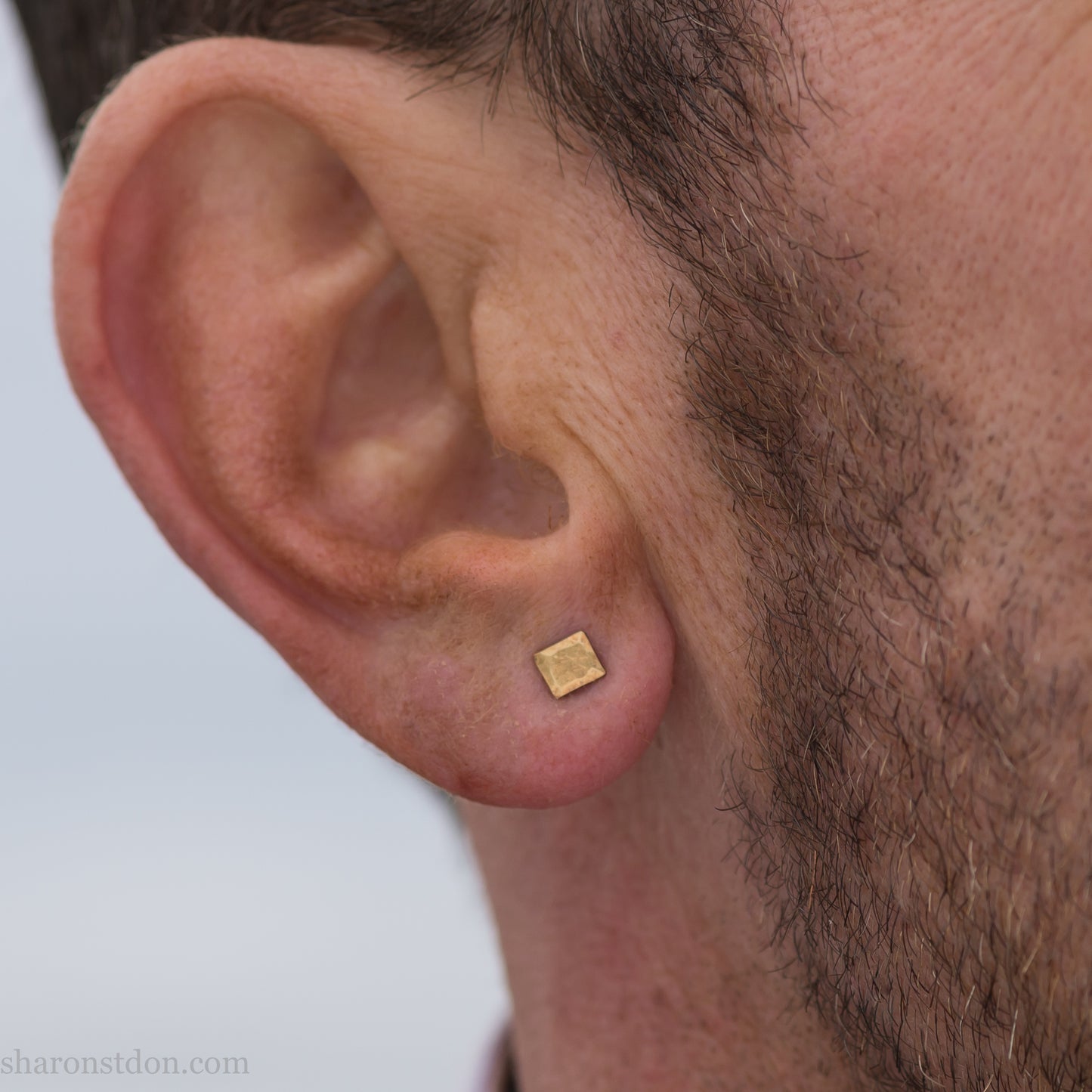 Handmade 22k gold and oxidized sterling silver stud earrings. 7mm square with hammered, matte texture finish. Handmade by Sharon Saint Don in USA. pictured on a man with brown hair, brown beard and fair skin.