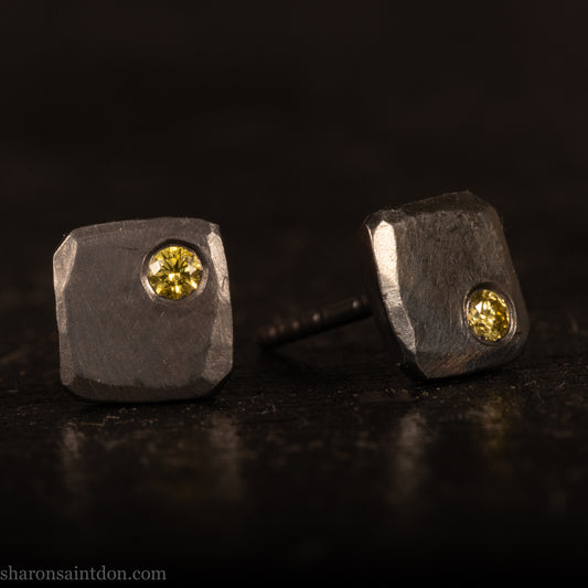 Handcrafted sterling silver square stud earrings with a 2mm canary yellow diamond set in the corner, hammered texture, oxidized black finish.