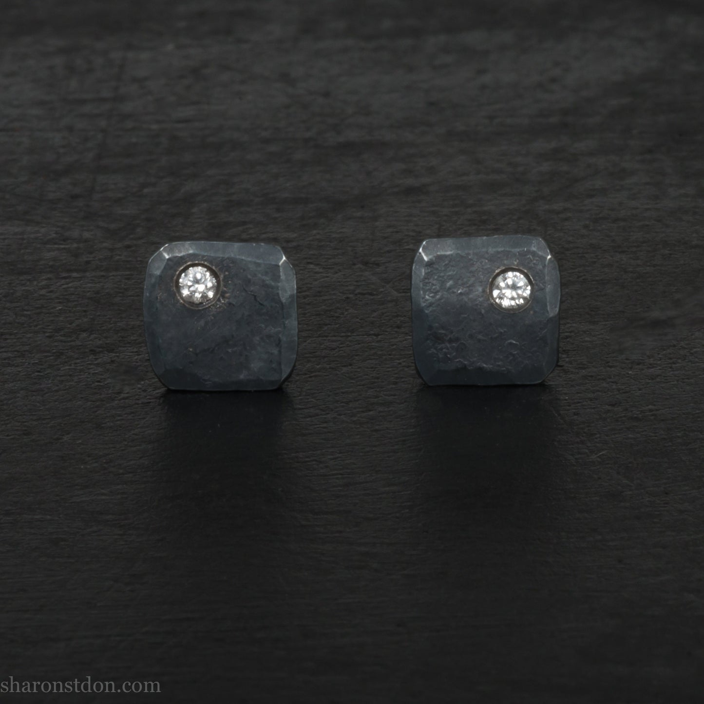 7mm square 925 sterling silver stud earrings with a 2 millimeter Canadian diamond gemstone in the corner. Hammered texture with a matte, charcoal, oxidized black finish. Handmade by Sharon SaintDon in North America.