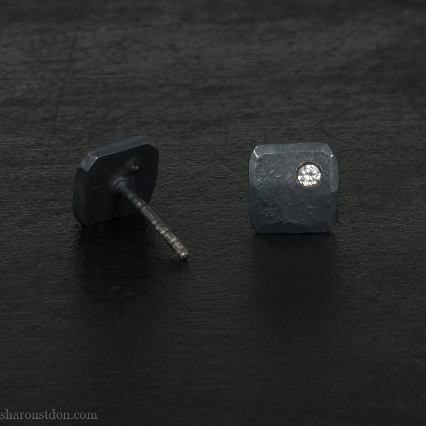 7mm square 925 sterling silver stud earrings with a 2 millimeter Canadian diamond gemstone in the corner. Hammered texture with a matte, charcoal, oxidized black finish. Handmade by Sharon SaintDon in North America.