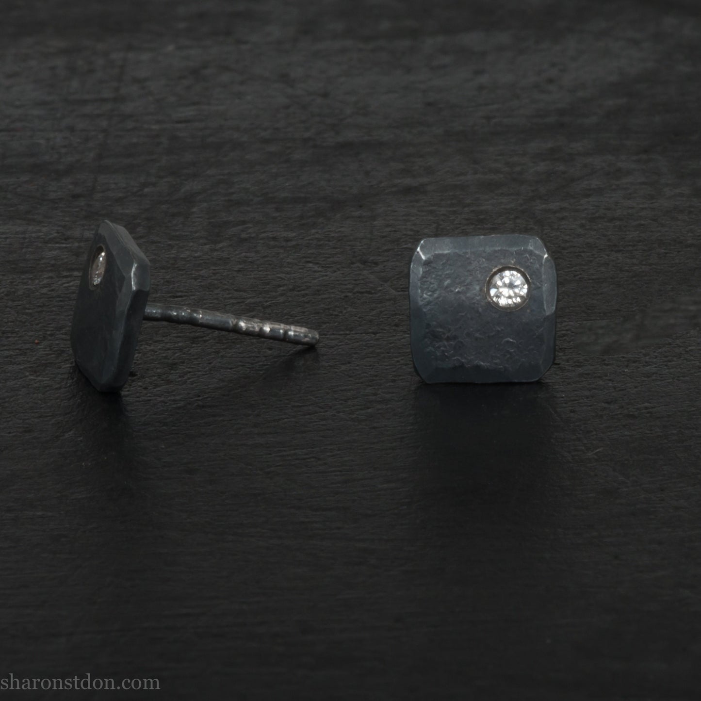 7mm square 925 sterling silver stud earrings with a 2 millimeter Canadian diamond gemstone in the corner. Hammered texture with a matte, charcoal, oxidized black finish. Handmade by Sharon SaintDon in North America.