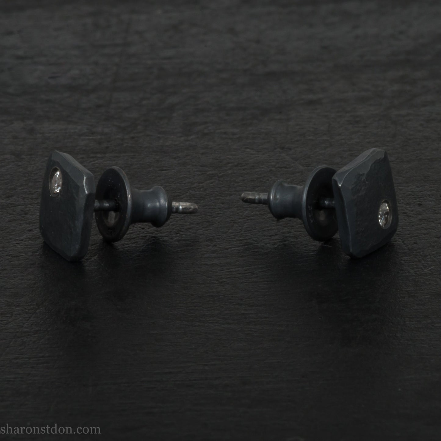 7mm square 925 sterling silver stud earrings with a 2 millimeter Canadian diamond gemstone in the corner. Hammered texture with a matte, charcoal, oxidized black finish. Handmade by Sharon SaintDon in North America.
