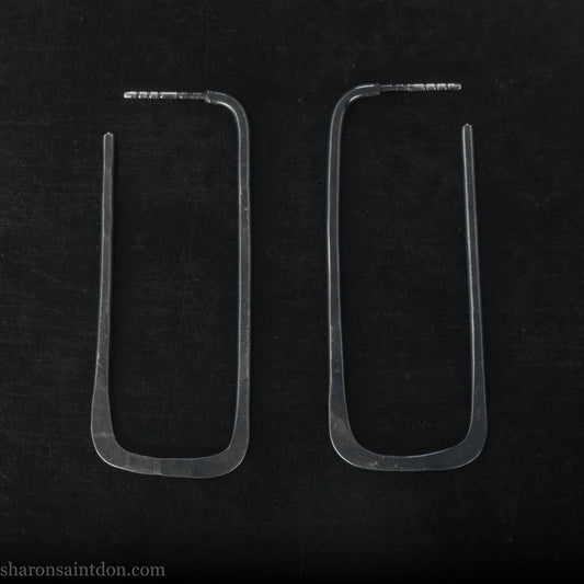 Person wearing hand hammered oxidized black rectangle hoop earrings in solid 925 sterling silver. 2x5cm, matte black patina.