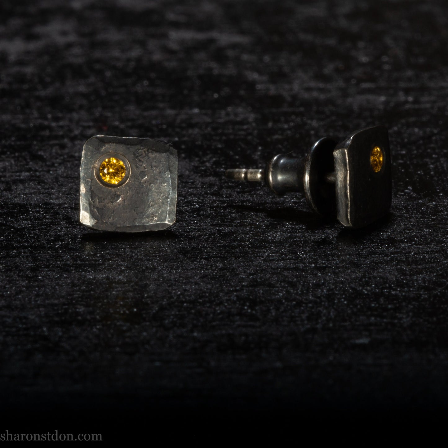 Handmade 925 sterling silver stud earrings handmade by Sharon SaintDon In North America. 7mm x 7mm hammered, square, oxidized black silver with a 2mm round lab grown golden yellow topaz gemstone in the corner.