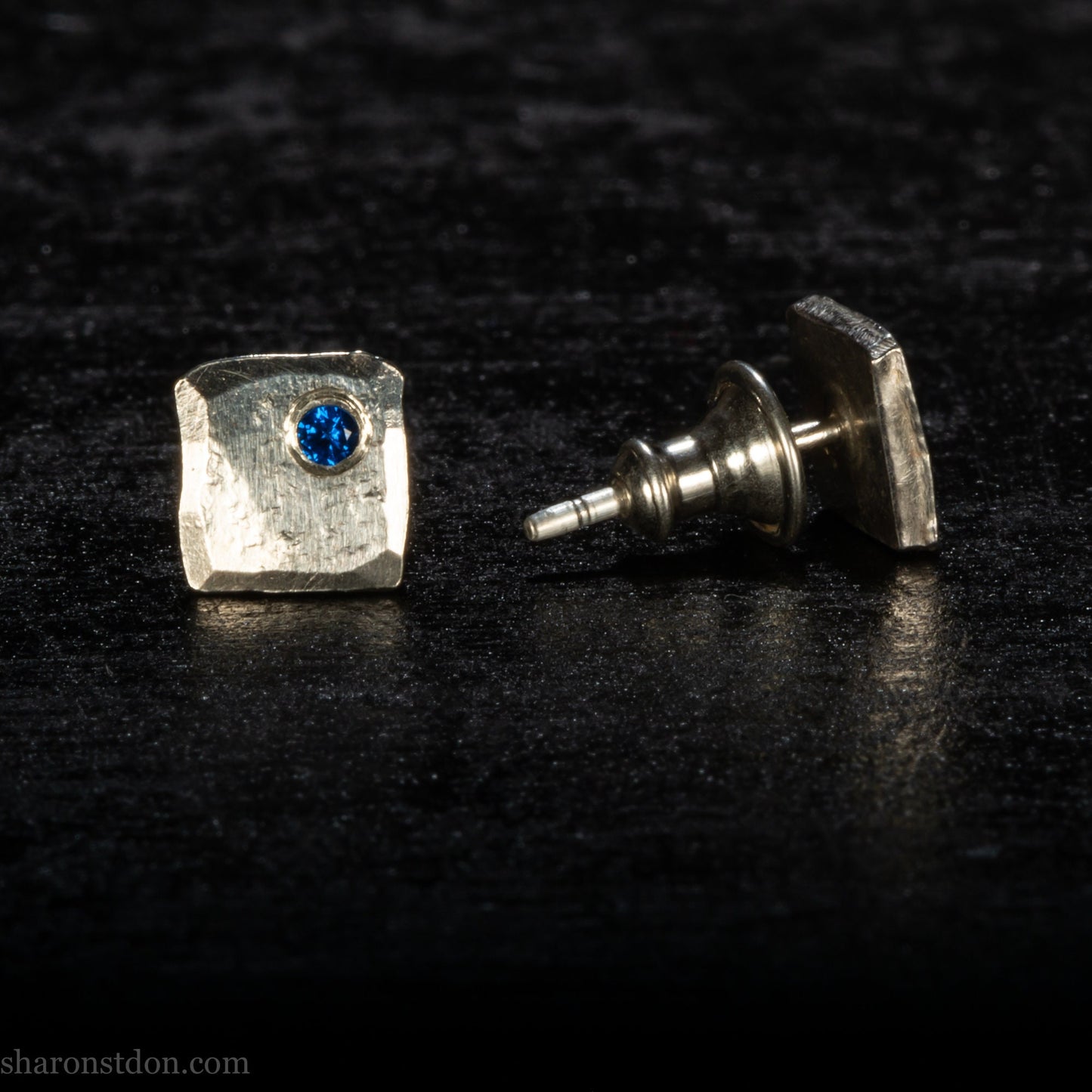 Handmade 925 sterling silver stud earrings for men with 2mm, lab grown blue spinel gemstone set in the corner. 7mm square, 1.5mm thick with silver posts and backs and hammered, matte, brushed finish. Handmade by Sharon SaintDon in North America.