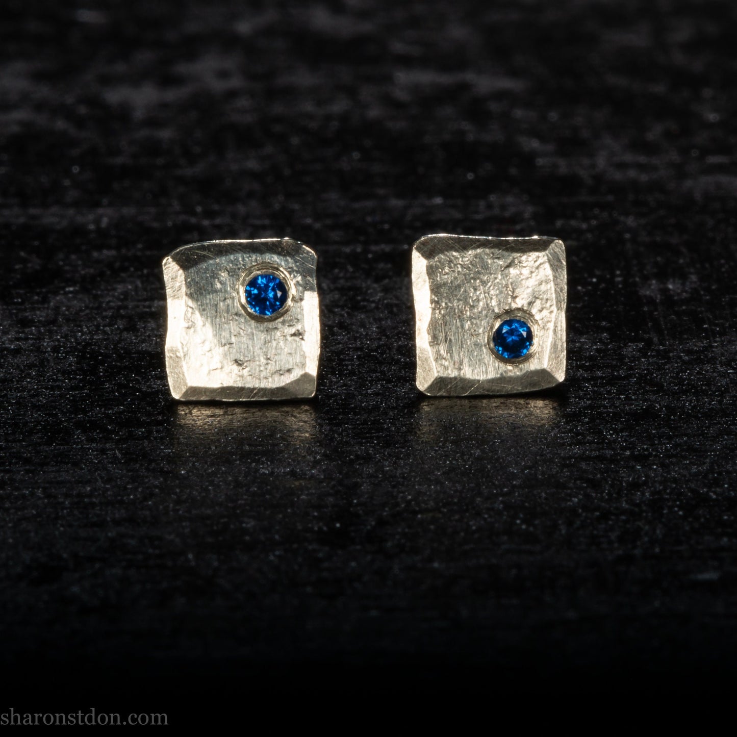 Handmade 925 sterling silver stud earrings for men with 2mm, lab grown blue spinel gemstone set in the corner. 7mm square, 1.5mm thick with silver posts and backs and hammered, matte, brushed finish. Handmade by Sharon SaintDon in North America.