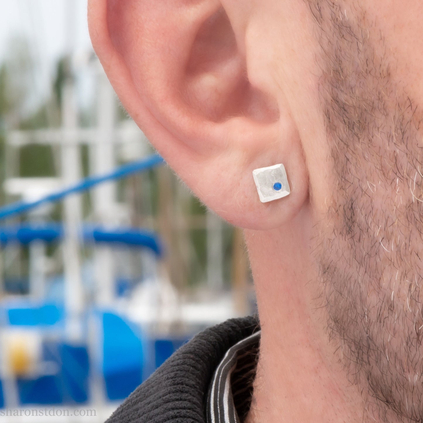 Handmade 925 sterling silver stud earrings for men with 2mm, lab grown blue spinel gemstone set in the corner. 7mm square, 1.5mm thick with silver posts and backs and hammered, matte, brushed finish. Handmade by Sharon SaintDon in North America.