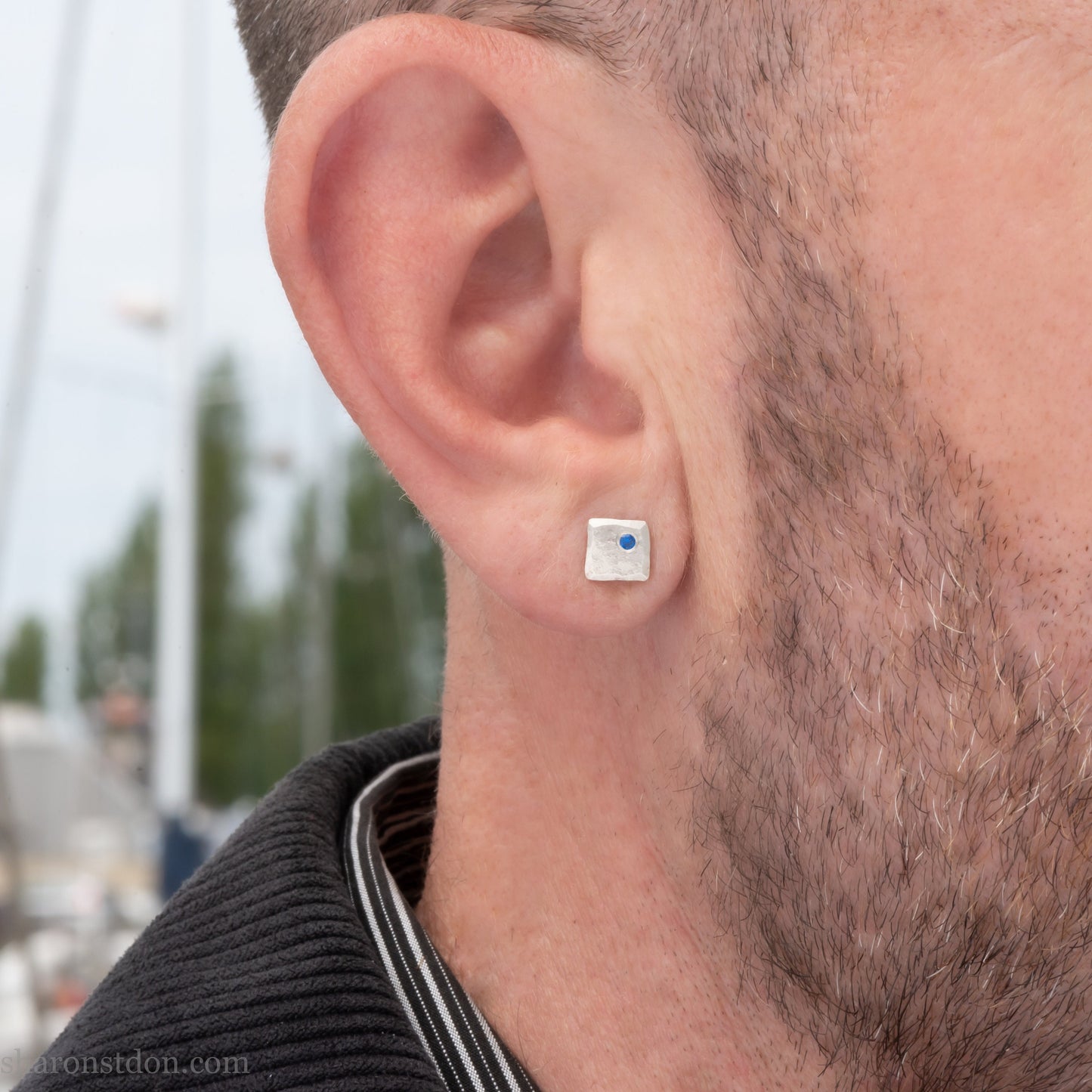 Handmade 925 sterling silver stud earrings for men with 2mm, lab grown blue spinel gemstone set in the corner. 7mm square, 1.5mm thick with silver posts and backs and hammered, matte, brushed finish. Handmade by Sharon SaintDon in North America.