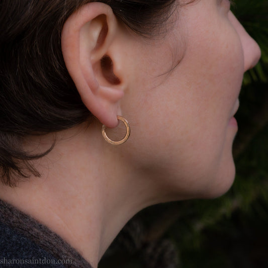 16mm diameter sold hoop earrings set handmade in North America by Sharon SaintDon. Hammered solid yellow gold, 2mm wide, 1.5mm thick, with 14k gold posts and locking backs.