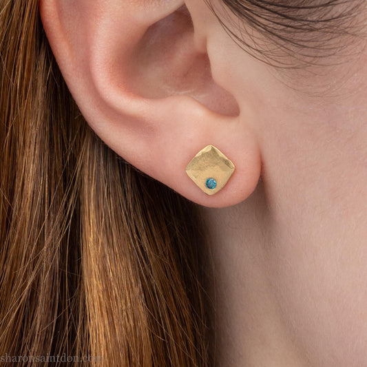 Hammered solid 18k yellow gold gemstone stud earrings with a 2mm teal blue diamond set in the corner. 7 x 7mm square x 1.5mm thick with a matte, brushed finish. Solid 18k gold posts and locking backs. Handmade by Sharon SaintDon in North America.