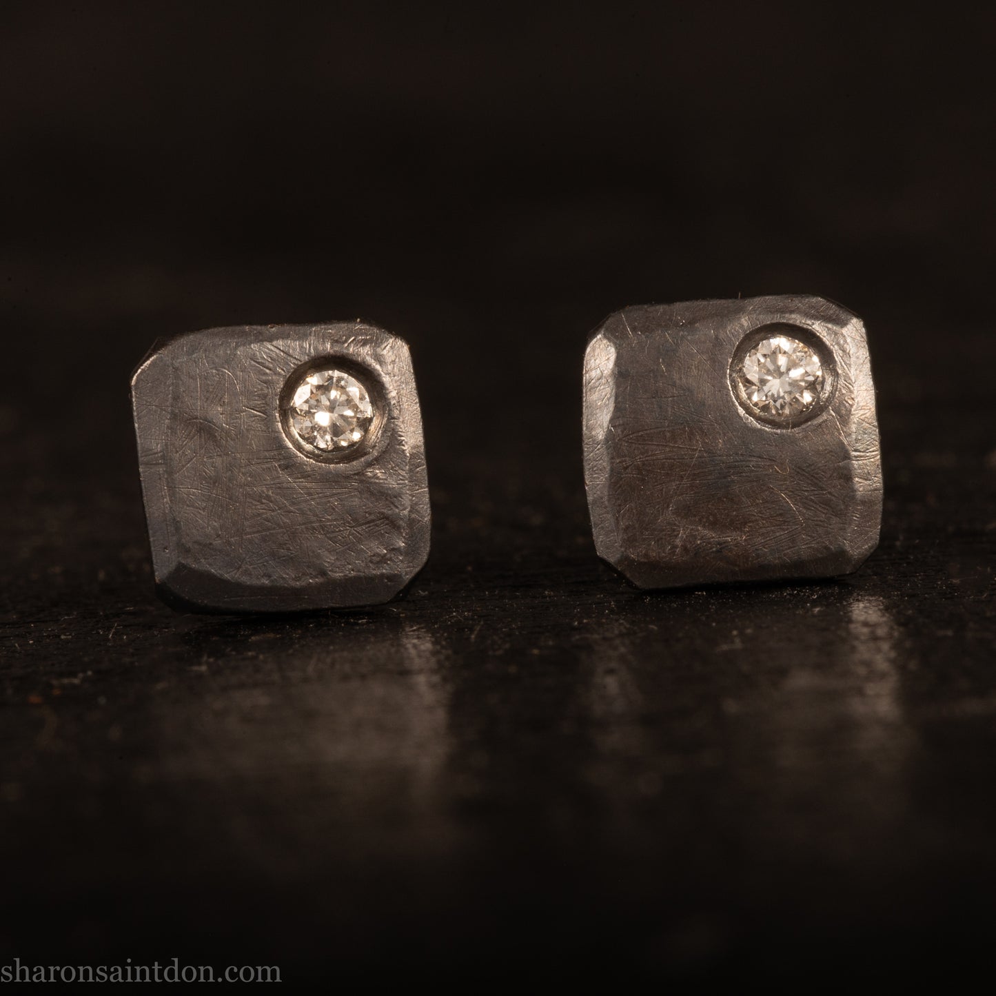 Handcrafted 925 sterling silver stud earrings with moissanite, lab grown, alternative diamond gemstones. 7mm square, 1.5mm thick, solid hammered silver with oxidized black finish. 2mm round moissanite is set in the corner, posts and backs are sterling silver.