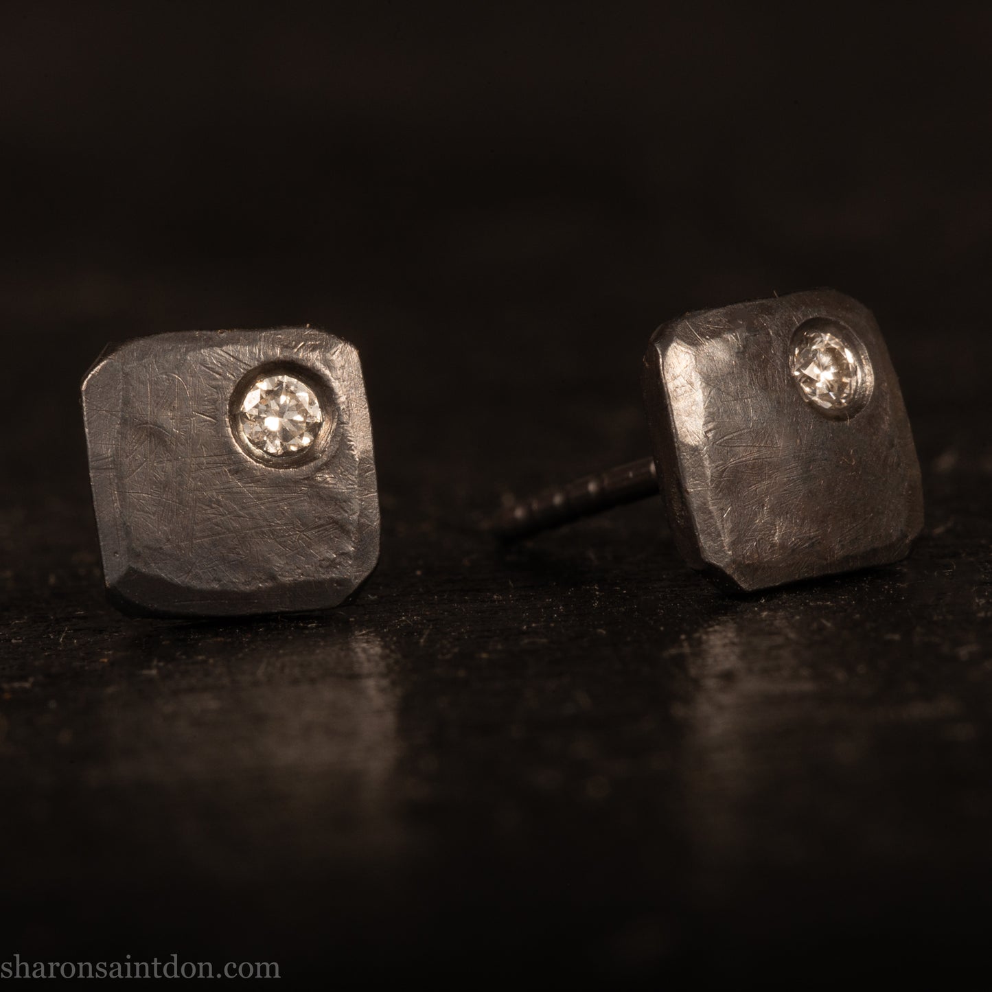 Handcrafted 925 sterling silver stud earrings with moissanite, lab grown, alternative diamond gemstones. 7mm square, 1.5mm thick, solid hammered silver with oxidized black finish. 2mm round moissanite is set in the corner, posts and backs are sterling silver.