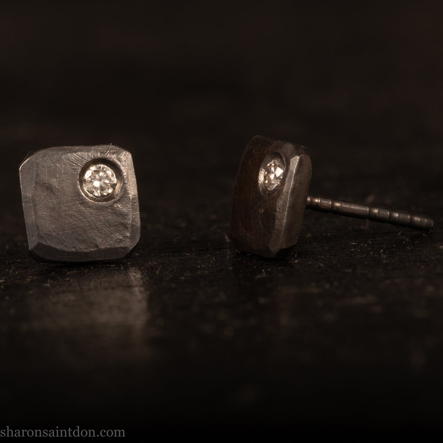 Handcrafted 925 sterling silver stud earrings with moissanite, lab grown, alternative diamond gemstones. 7mm square, 1.5mm thick, solid hammered silver with oxidized black finish. 2mm round moissanite is set in the corner, posts and backs are sterling silver.