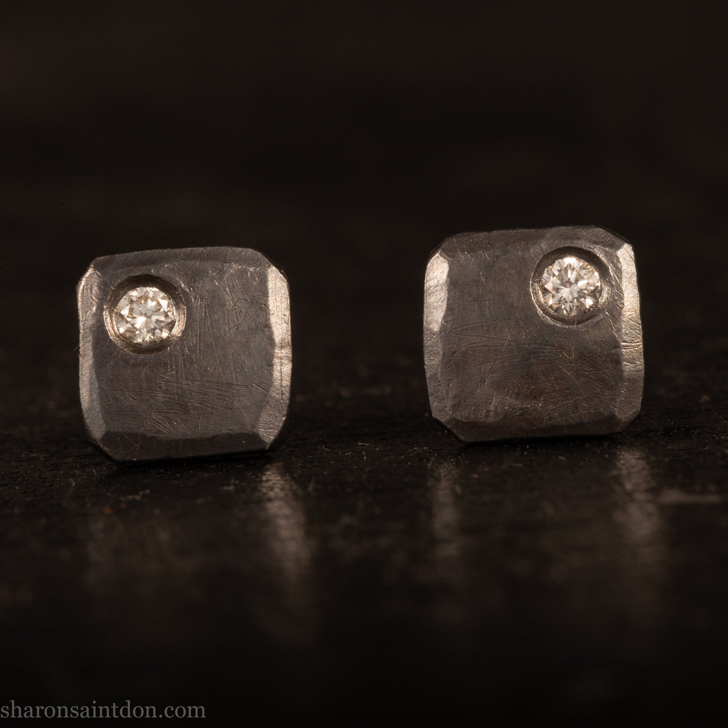 Handcrafted 925 sterling silver stud earrings with moissanite, lab grown, alternative diamond gemstones. 7mm square, 1.5mm thick, solid hammered silver with oxidized black finish. 2mm round moissanite is set in the corner, posts and backs are sterling silver.