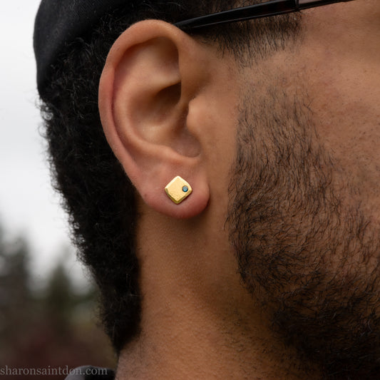 Solid yellow gold square stud earrings with 2mm blue diamonds, matte finish, shown worn on a model with a beard (side view, one ear).