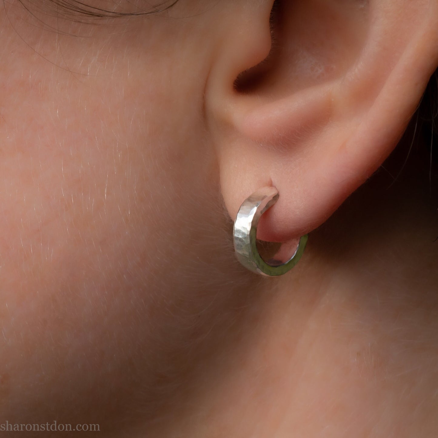 Hammered solid 925 silver hoop earrings with a matte shiny finish. 12mm exterior diameter, 9mm interior, 3mm wide and 1.5mm thick. Solid sterling silver posts and backs. Handcrafted by Sharon Saint Don in the USA. Pictured on a fair skinned person.