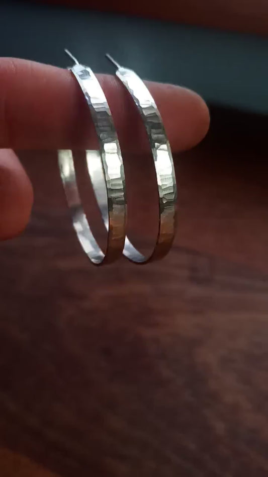 Large, solid sterling silver hoop earrings. Handmade in North America by Sharon SaintDon. 50mm diameter x 5mm wide, .75mm thick. Hammered, wavy, texture with a matte brushed finish, silver posts and backs.