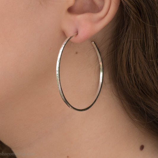 Solid 925 sterling silver hoop earrings. 50mm diameter, 2mm wide, 1.5mm thick with a matte, shiny finish. Lightweight hammered large hoop earrings handmade by Sharon SaintDon in North America.