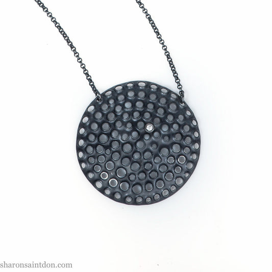 Handmade, large, 925 sterling silver pendant necklace by Sharon SaintDon. 50mm diameter round, covered in perforated holes, oxidized black with cubic zirconia gemstone. 36 or 18 inch black chain.