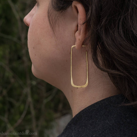 Large gold hoop earrings handmade by Sharon SaintDon in the Pacific Northwest of North America. Hand forged solid 18k yellow gold rectangles, 2cm wide x 5cm long with a matte brushed finish. The locking backs and posts are also solid 18k gold.