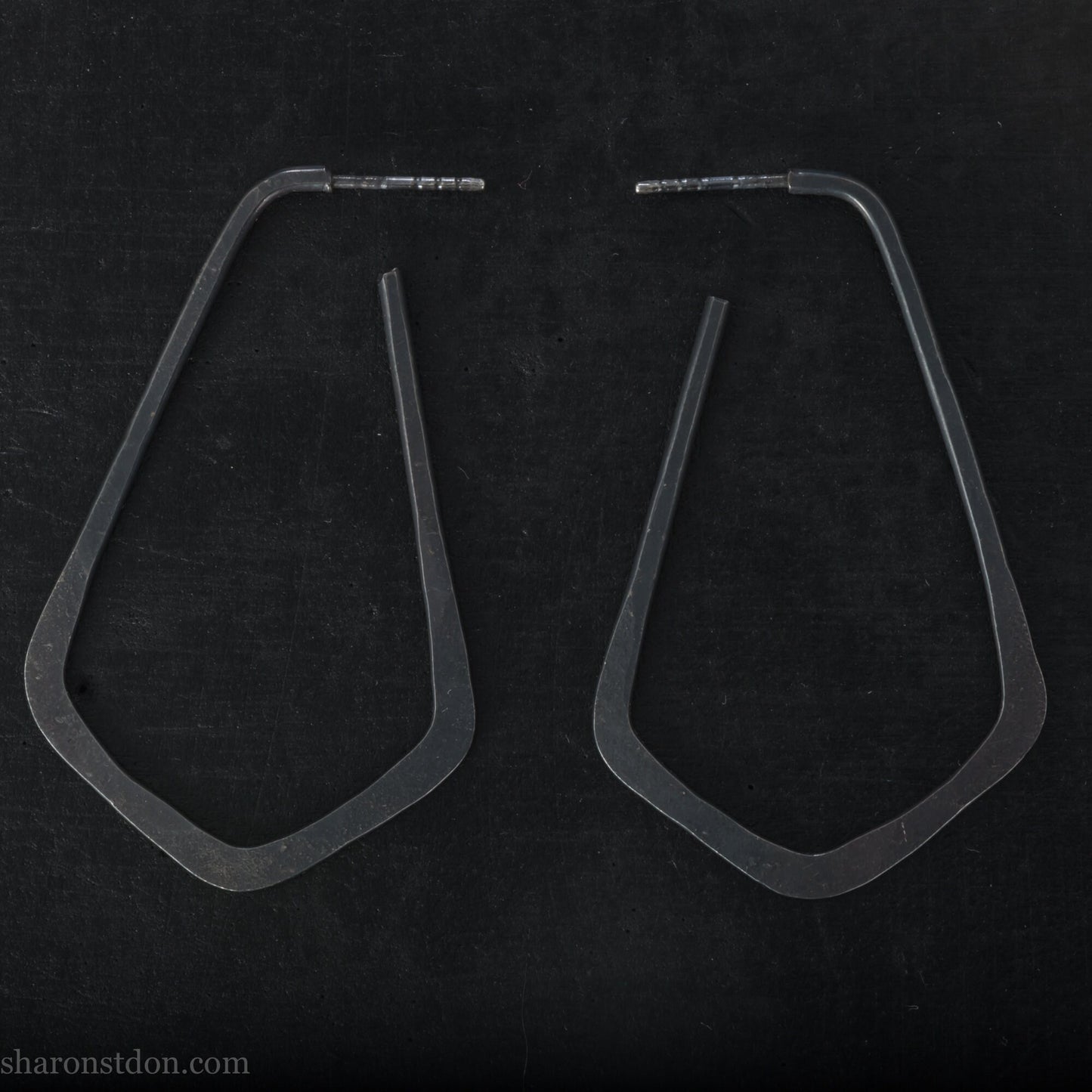 925 sterling silver hoop earrings handmade in North America by Sharon SaintDon. Long, angular, teardrop shape with three points at bottom, oxidized black with hammered texture. SIZE: 5cm high x 32mm wide