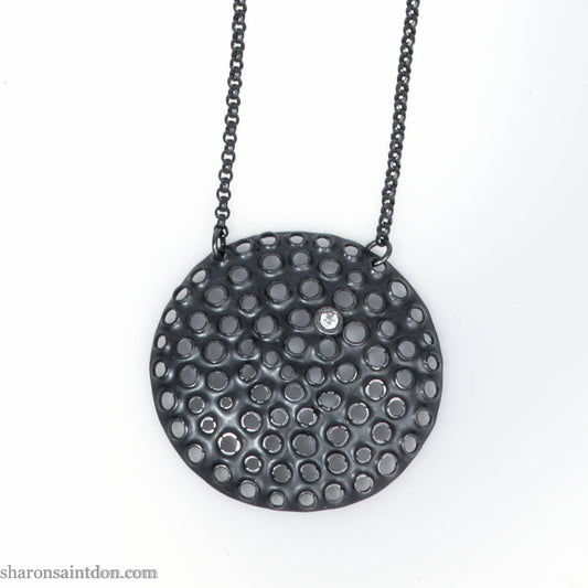 Handmade, large, 925 sterling silver pendant necklace by Sharon SaintDon. 50mm diameter round, covered in perforated holes, oxidized black with cubic zirconia gemstone. 36 or 18 inch black chain.