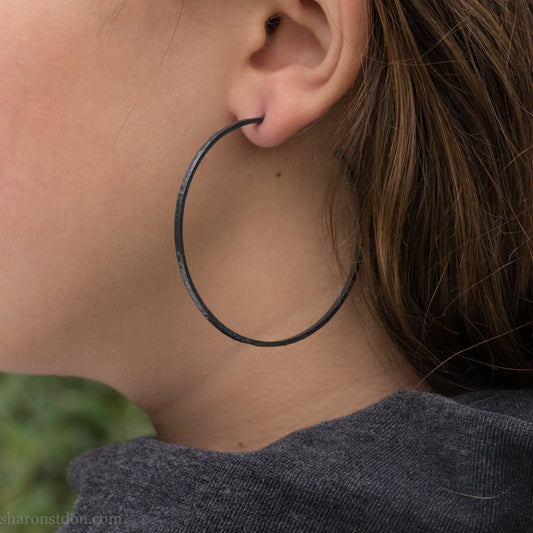 Handmade 925 sterling silver hoop earrings for women. 55mm diameter, 2mm wide, oxidized black, large hoops for daily wear. Minimalist, comfortable, lightweight with a hammered, texture.