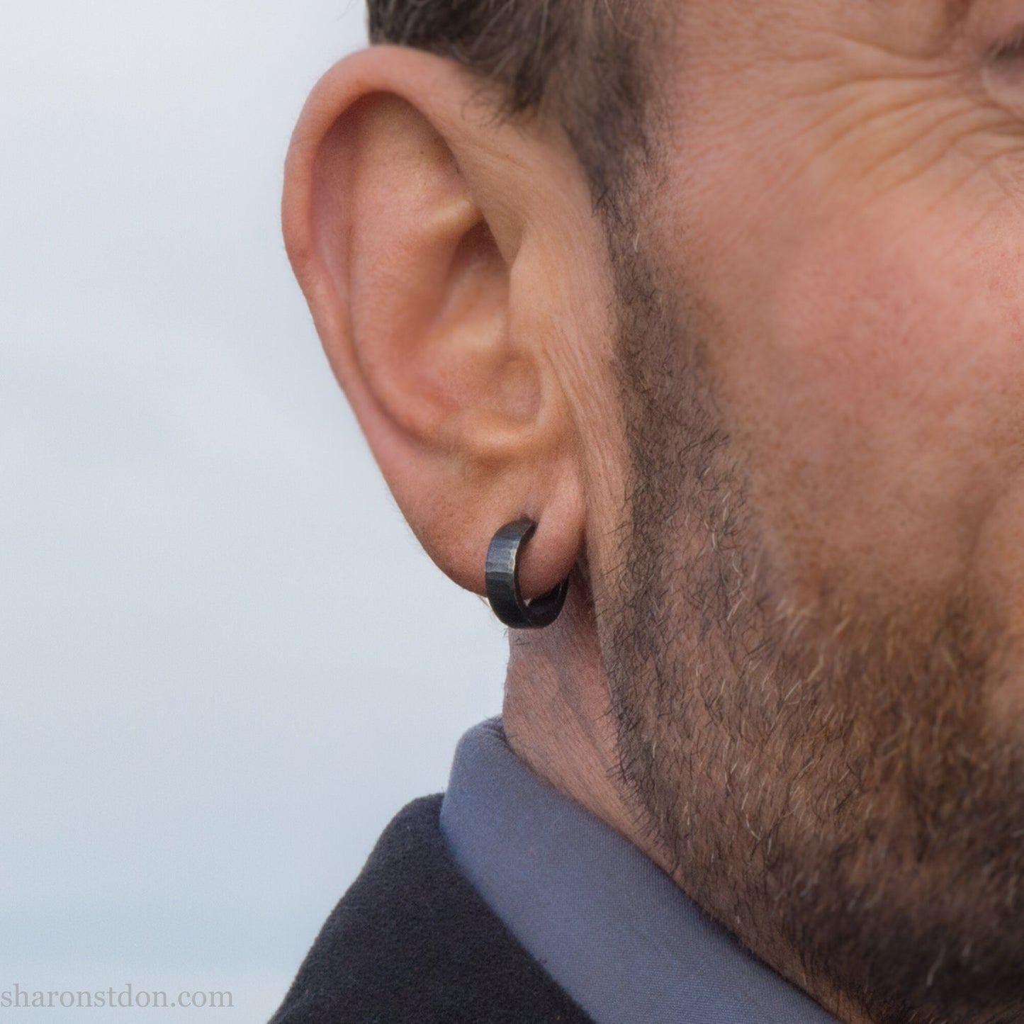 Close up photo of a man wearing handcrafted oxidized black 14mm x 4mm hammered solid sterling silver hoop earrings.