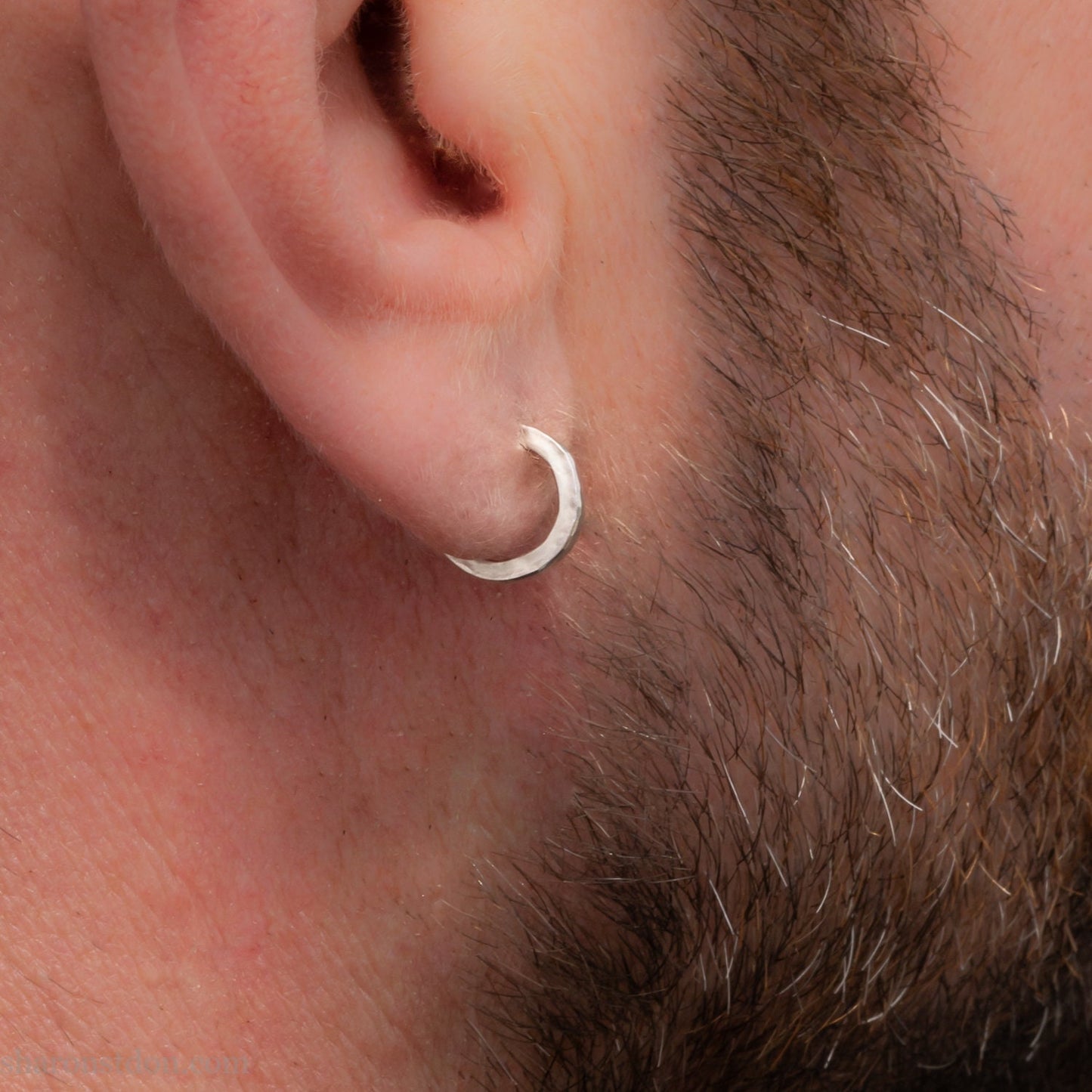 Man with light skin and brown beard wearing handcrafted solid sterling silver hoop earrings, with a hammered texture and a matte, brushed, shiny finish. SIZE: 12mm exterior diameter, 9mm interior, 2mm wide. and 1.5mm thick.