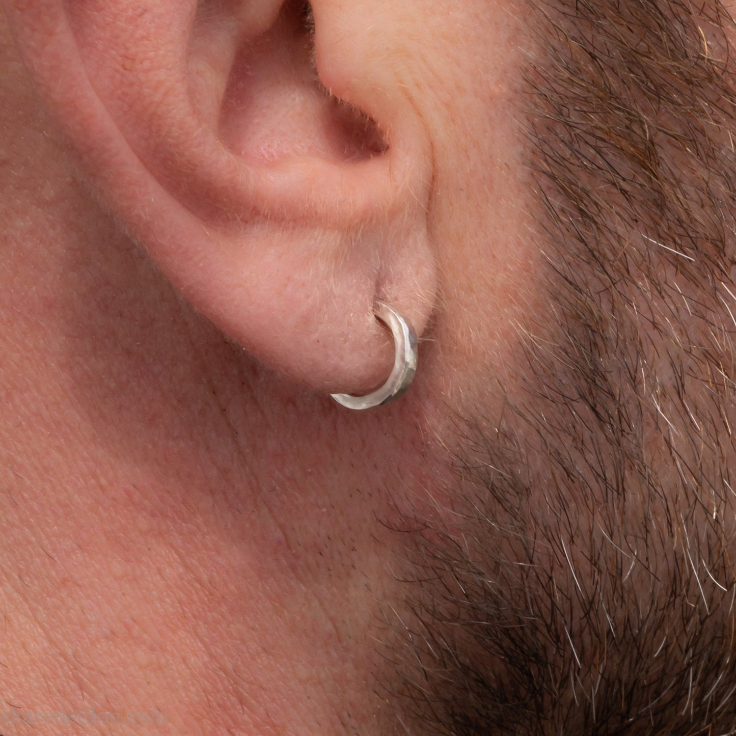Handmade solid sterling silver hoop earrings, hammered by hand with a matte, brushed, shiny finish. SIZE: 12mm exterior diameter, 9mm interior, 2mm wide. and 1.5mm thick. Pictured on a man with light skin and brown beard.