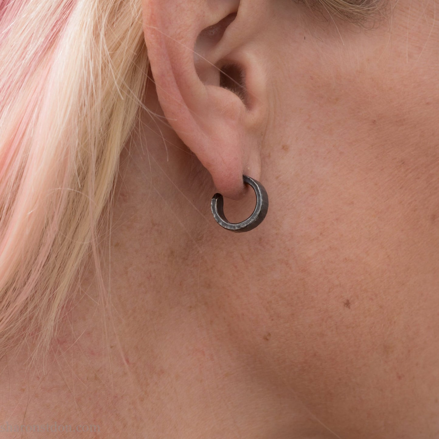 Close up photo of a woman wearing oxidized black 14mm x 4mm hammered solid sterling silver hoop earrings.