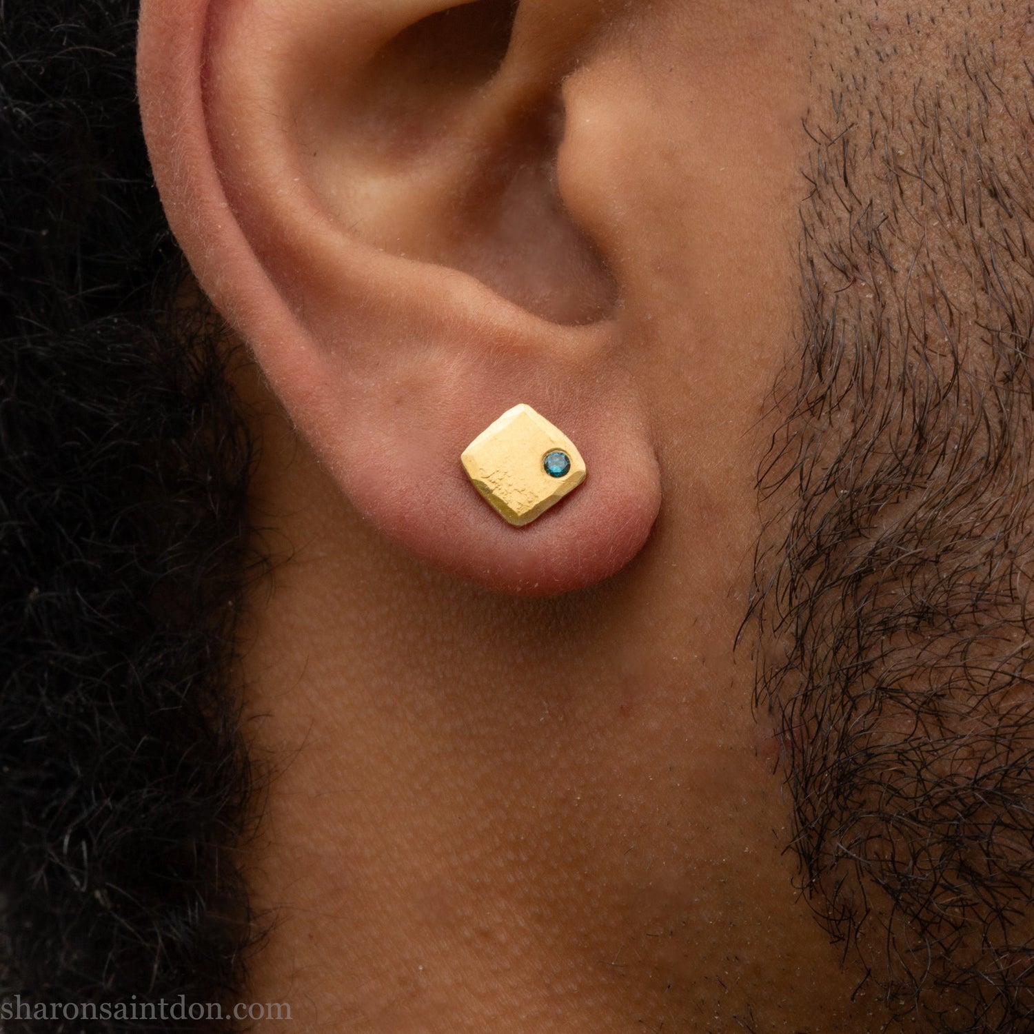 Solid 18k yellow gold stud earrings with a 2mm blue diamonds. 7 x 7mm square x 1.5mm thick with a matte finish. Solid 18k gold posts and locking backs. Handcrafted in the USA by Sharon Saint Don. Modeled by a man with dark skin, black beard and hair.