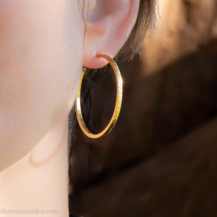 Solid hammered yellow gold hoop earrings with a matte, brushed finish, close up image on a model. 35mm diameter, 2mm wide.