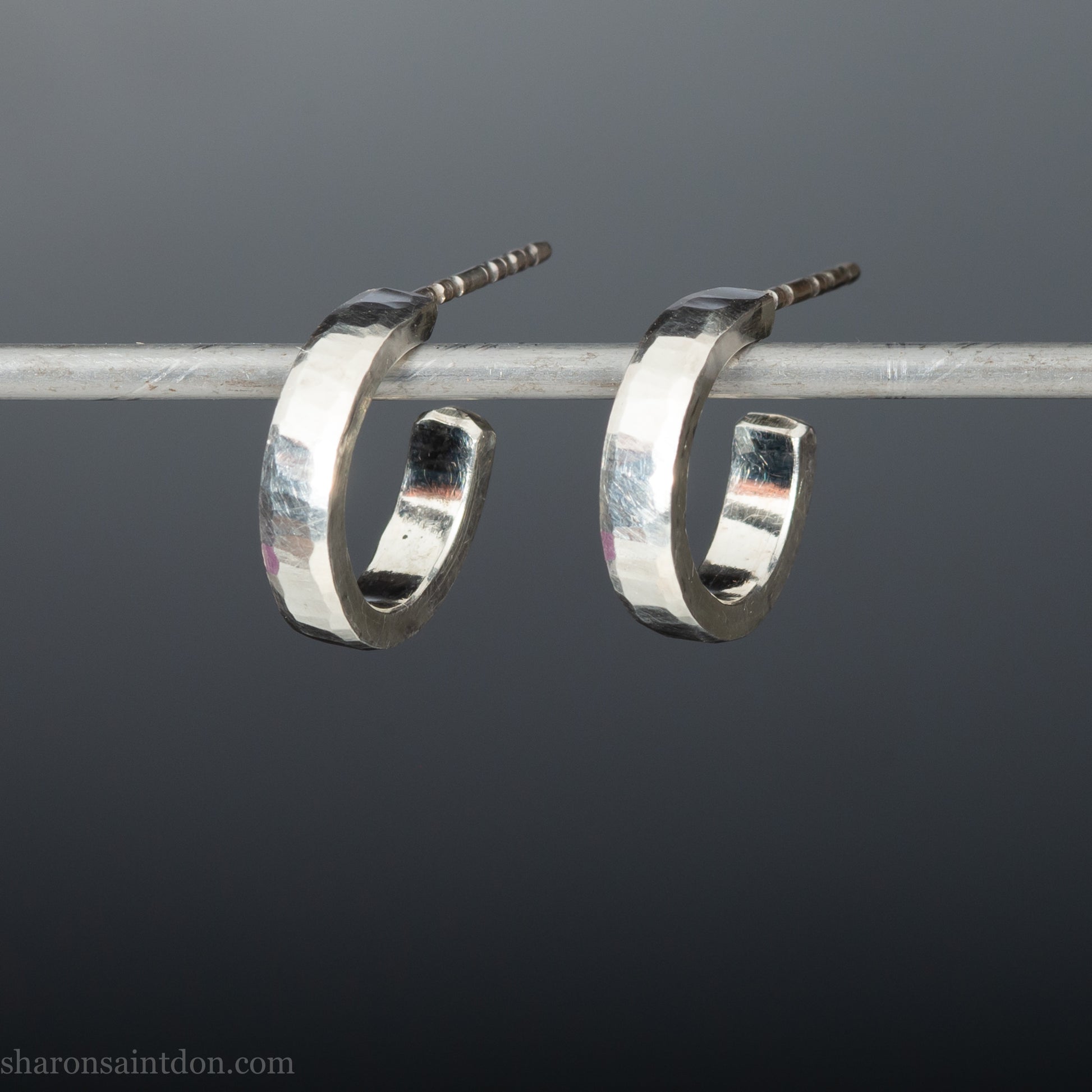 A close-up view of handcrafted solid silver hoop earrings, 14mm diameter x 3mm wide x 1.5mm thick with a hammered matte finish.