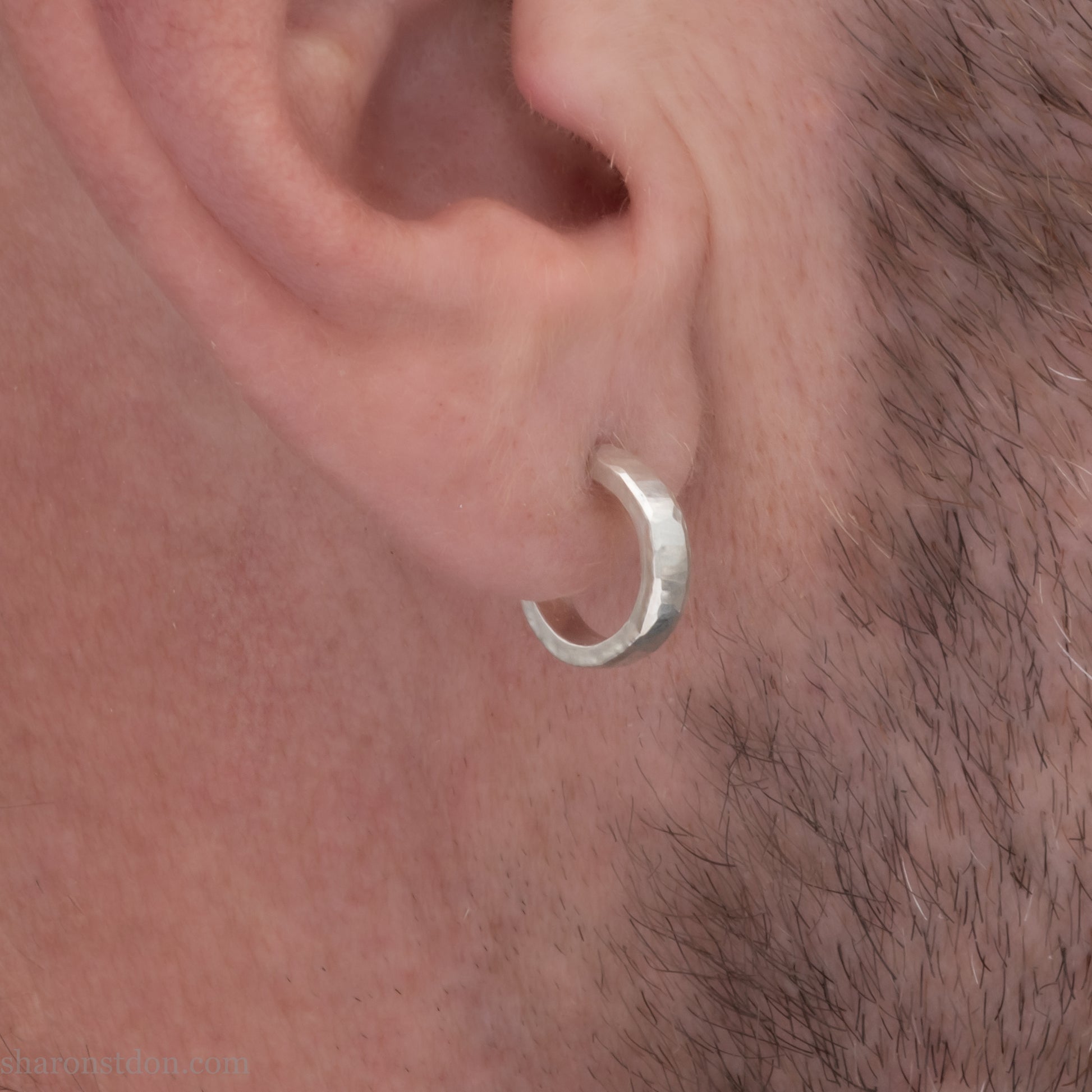 A close-up view of a man wearing handcrafted solid silver hoop earrings, 14mm diameter x 3mm wide x 1.5mm thick with a hammered matte finish.