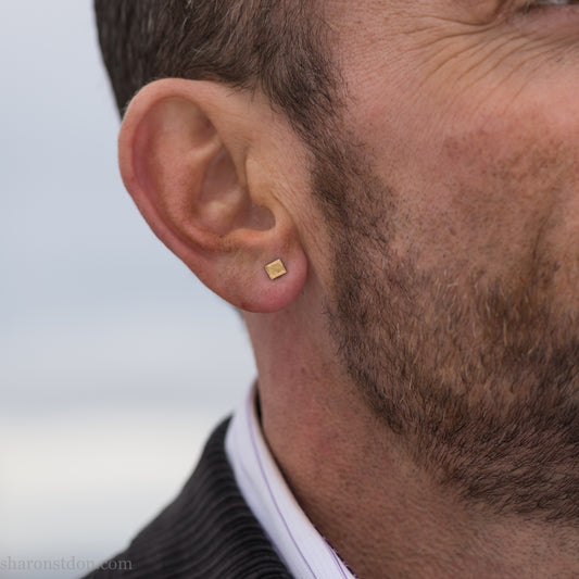 Handmade 22k gold and oxidized sterling silver stud earrings. 7mm square with hammered, matte texture finish. Handmade by Sharon Saint Don in USA. pictured on a man with brown hair, brown beard and fair skin.