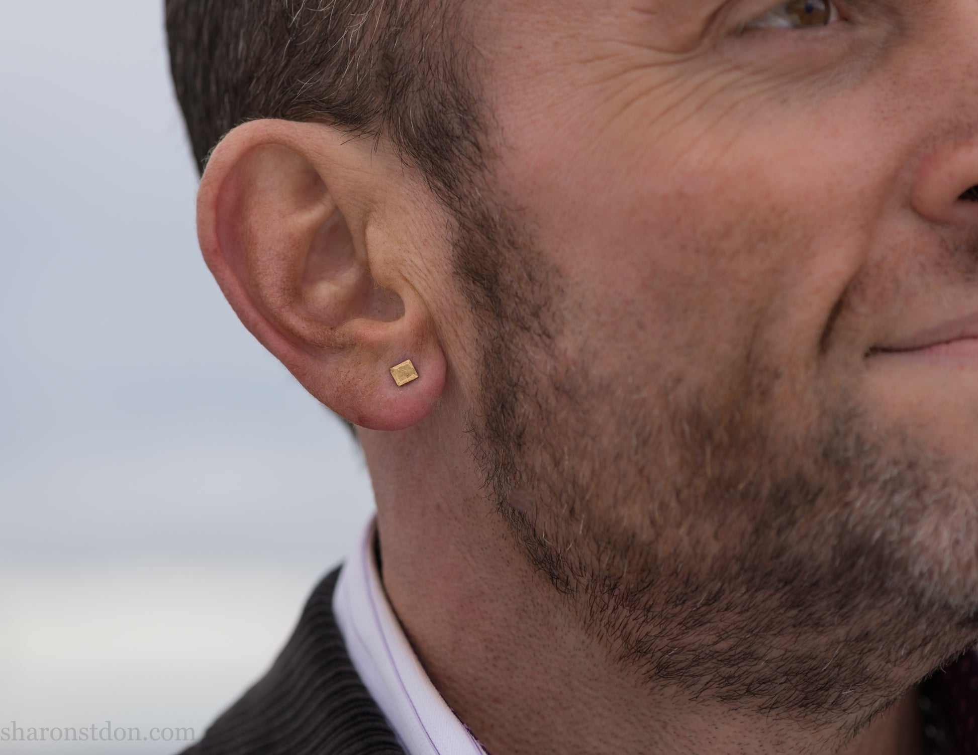 Handmade 22k gold and oxidized sterling silver stud earrings. 7mm square with hammered, matte texture finish. Handmade by Sharon Saint Don in USA. pictured on a man with brown hair, brown beard and fair skin.