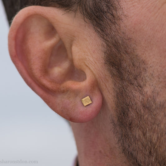 Handmade 22k gold and oxidized sterling silver stud earrings. 7mm square with hammered, matte texture finish. Handmade by Sharon Saint Don in USA. pictured on a man with brown hair, brown beard and fair skin.