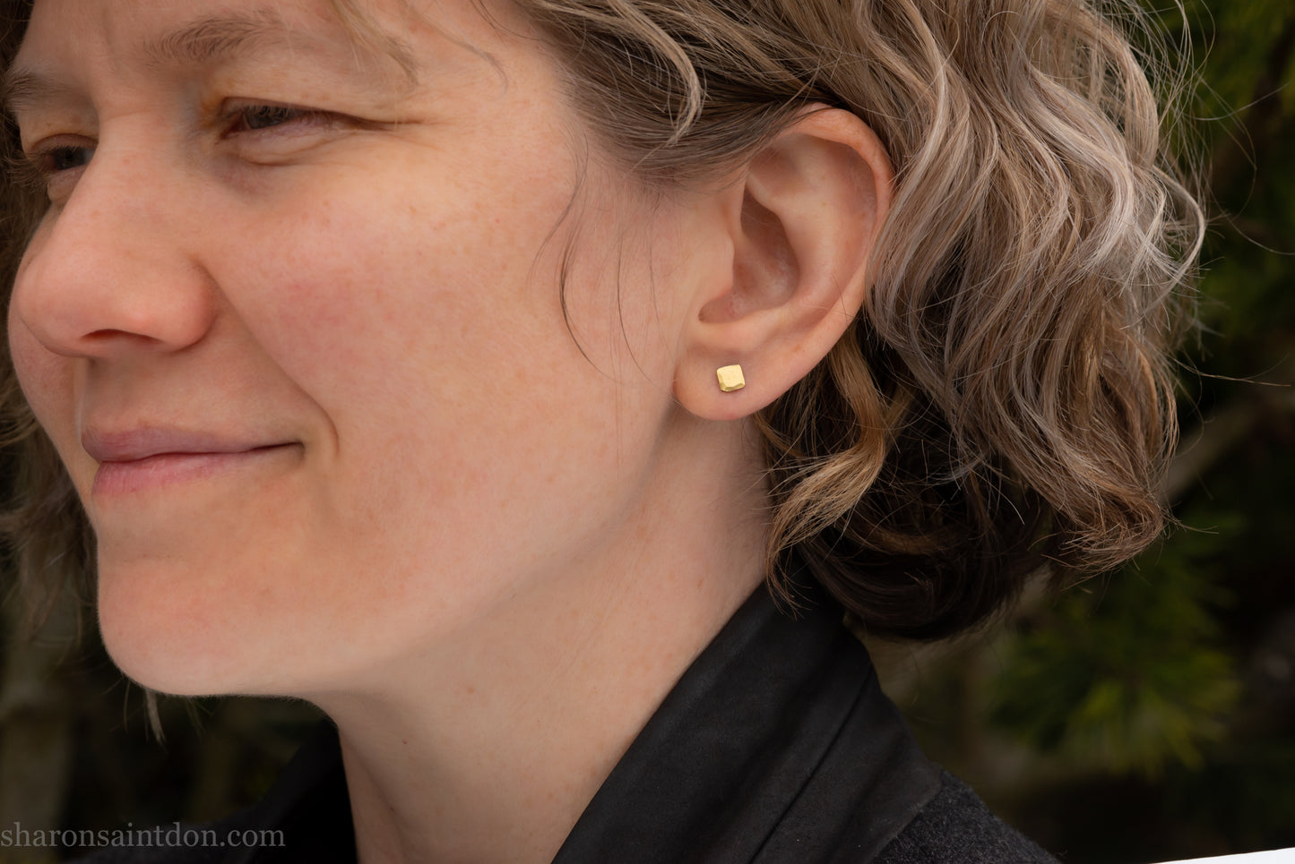 Handmade 22k gold and oxidized sterling silver stud earrings. 7mm square with hammered, matte texture finish. Handmade by Sharon Saint Don in USA. pictured on a person with light brown wavy hair, and fair skin.
