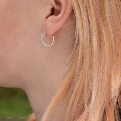 A close-up view of a person wearing a handcrafted solid silver hoop earring, 14mm diameter x 3mm wide x 1.5mm thick with a hammered matte finish.