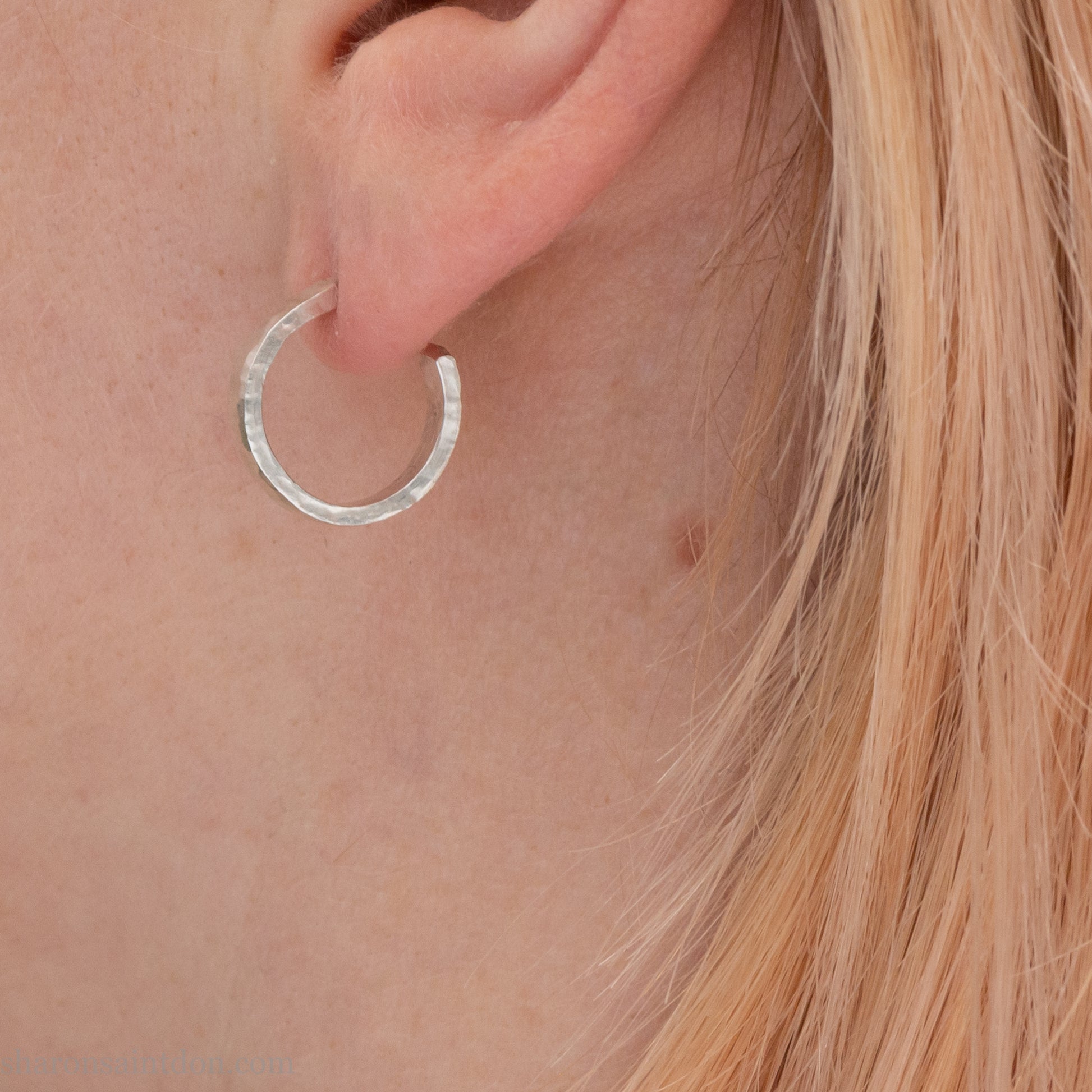 A close-up view of a person wearing a handcrafted solid silver hoop earring, 14mm diameter x 3mm wide x 1.5mm thick with a hammered matte finish.