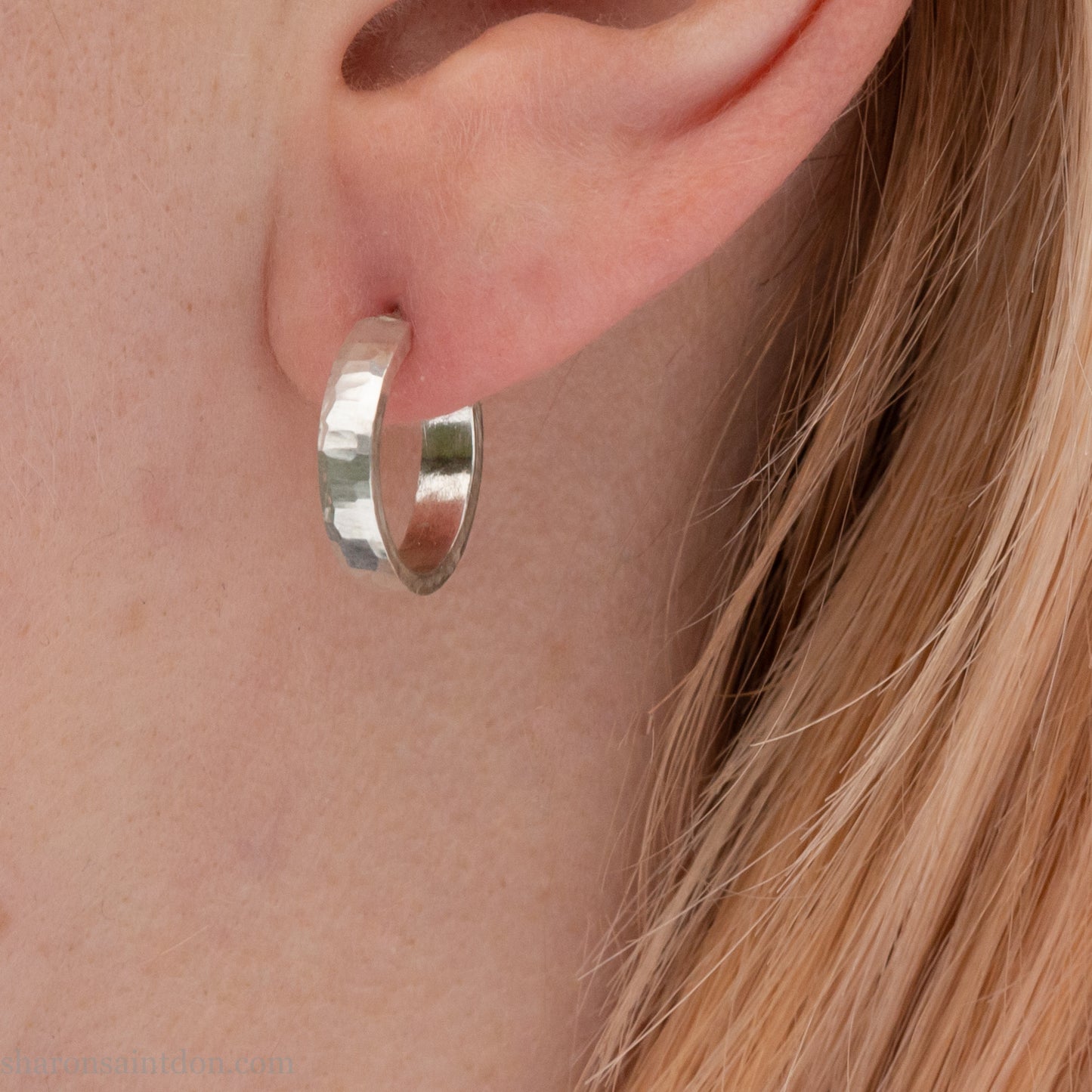 A close-up view of a person wearing handcrafted solid silver hoop earrings, 14mm diameter x 3mm wide x 1.5mm thick with a hammered matte finish.