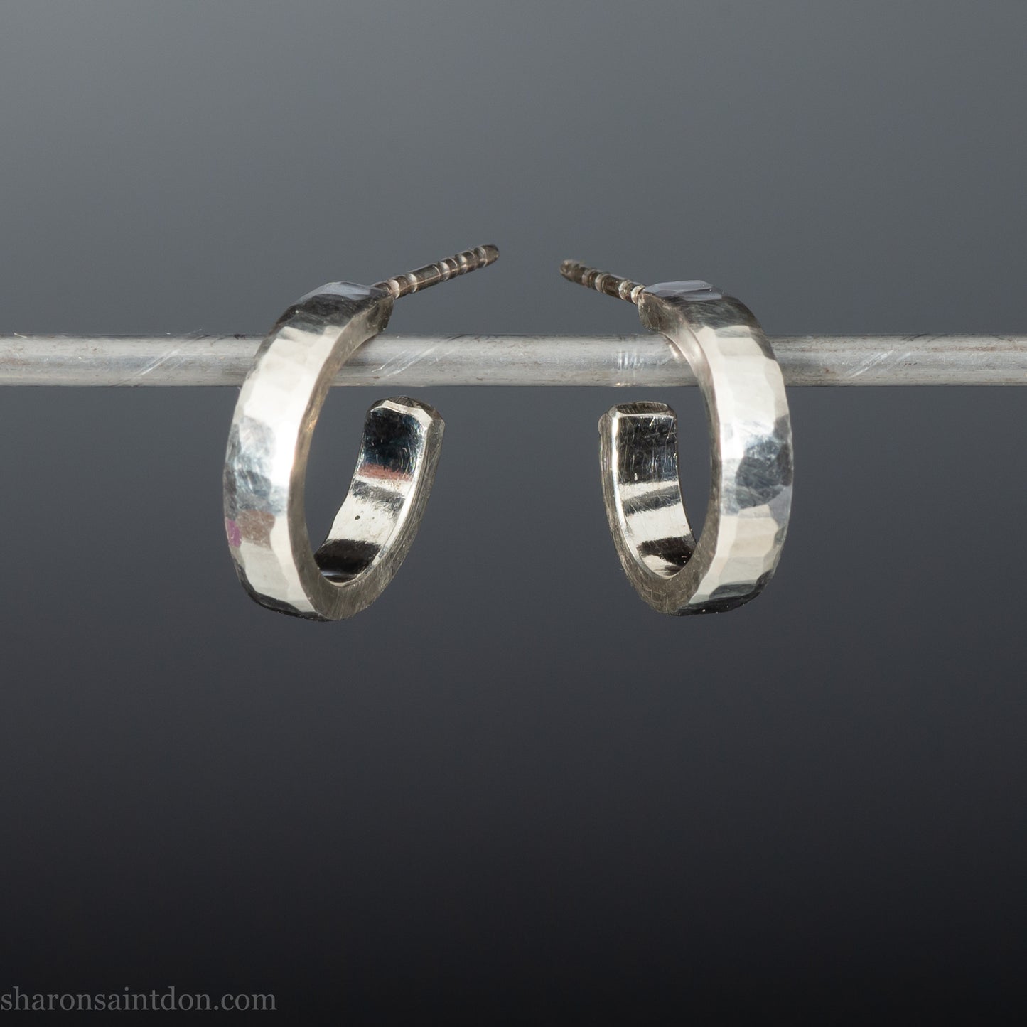 A close-up view of handcrafted solid silver hoop earrings, 14mm diameter x 3mm wide x 1.5mm thick with a hammered matte finish.