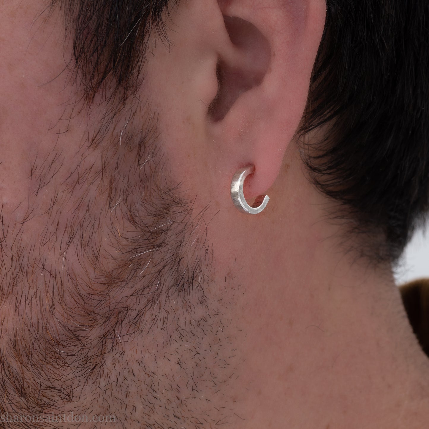 A close-up view of a person wearing handcrafted solid silver hoop earrings, 12mm diameter x 3mm wide x 1.5mm thick with a hammered matte finish.