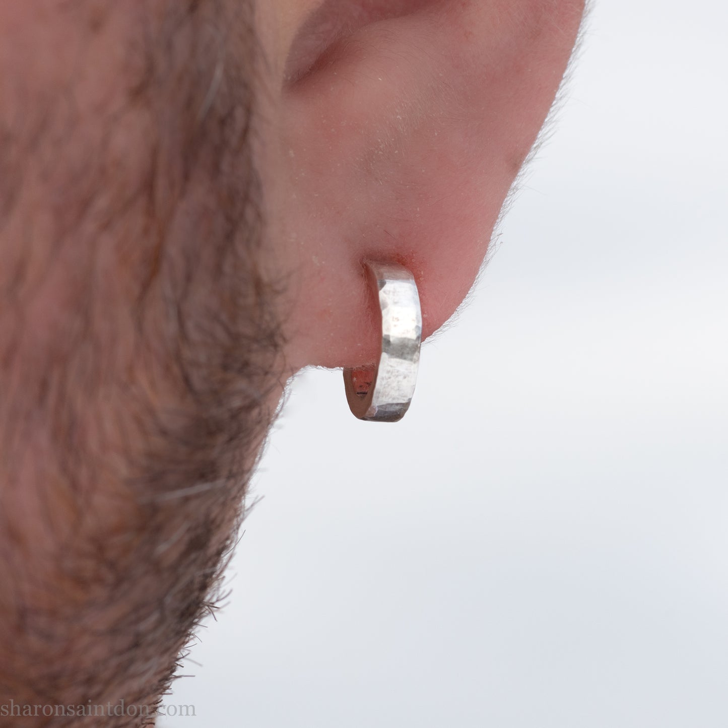 A close-up view of a person wearing handcrafted solid silver hoop earrings, 12mm diameter x 3mm wide x 1.5mm thick with a hammered matte finish.